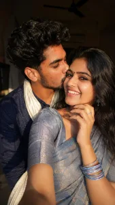 Ultra-realistic romantic selfie portrait of a young South Indian couple in warm natural sunlight. Beautiful South Indian girl with long silky black hair, soft smile, glowing skin, tiny bindi on forehead, wearing a shimmering silver-blue saree and bangles. Young South Indian boy with thick fluffy curly black hair, wearing a dark blue traditional kurta and white shawl, gently kissing her cheek. Close-up selfie composition, girl's hand resting on her chin with stylish dark nail polish and ring. Soft golden sunlight illuminating their faces, realistic skin texture, shallow depth of field, cozy indoor background with dark shadows and ceiling fan visible. Dreamy romantic mood, candid moment, high detail photography, cinematic color grading, DSLR quality, ultra sharp focus, natural facial expressions, Instagram story aesthetic, realistic lighting, 4K, portrait orientation 9:16.
Text Overlay (optional):
"கொழுத்து போன பொண்ணு இருந்தா கொண்டாடி..!" 🖤😘🙈
Negative Prompt:
blurry, low quality, extra fingers, deformed face, duplicate people, cartoon, painting, CGI, watermark, text errors, oversaturated colors, distorted hands, unrealistic skin, bad anatomy, cropped face, noise, artifacts. real face